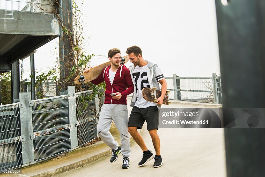 Two friends walking with skateboards and cell phone