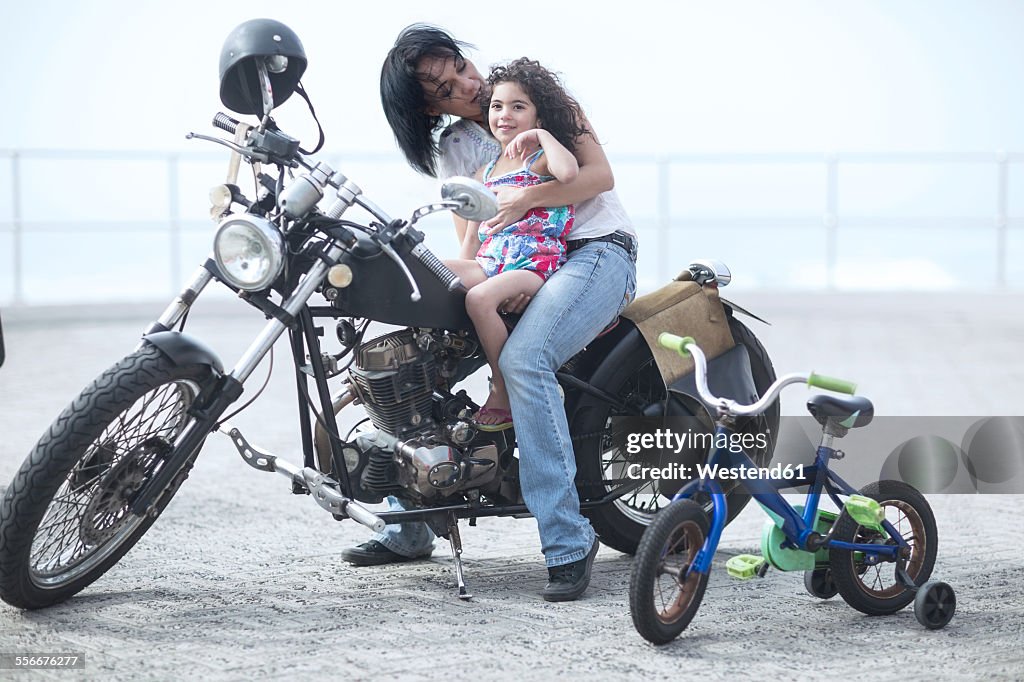 Mother and daughter sitting on motorcycle next to bike with training wheels