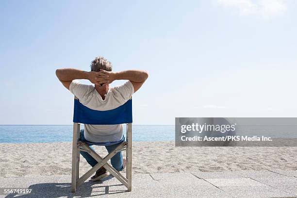 man relaxes in beach chairs, looks out to sea - mann von hinten stock-fotos und bilder