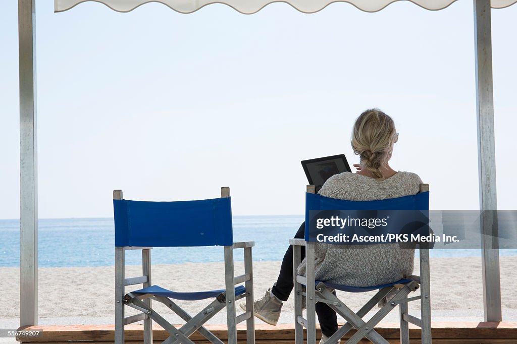 Woman relaxes in beach chairs, uses digital tablet