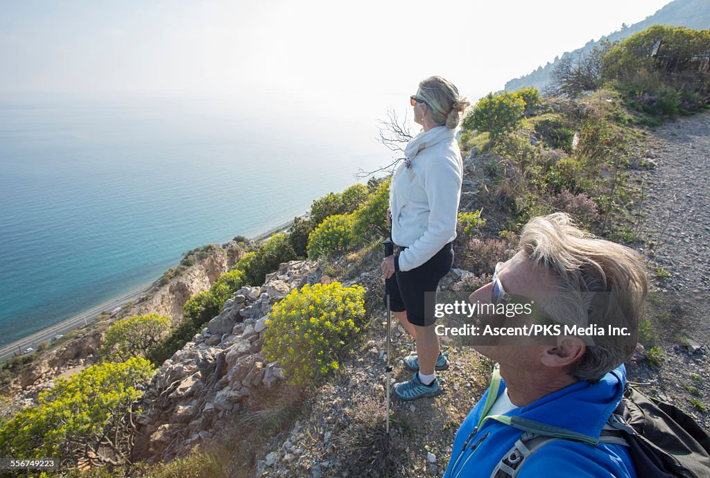 Hiking couple relax by trail, look out across sea
