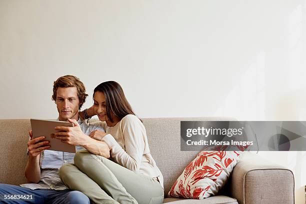 couple using digital tablet on sofa at home - pareja de mediana edad fotografías e imágenes de stock