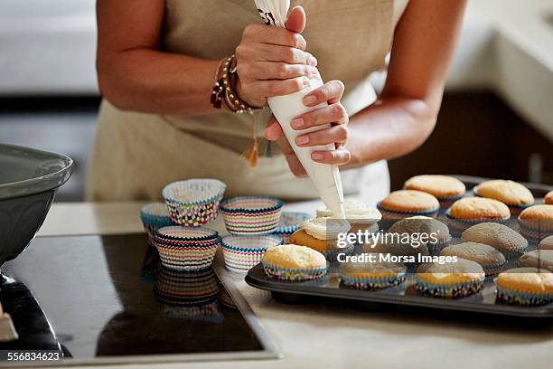 woman icing cupcakes at kitchen counter - alcorza fotografías e imágenes de stock