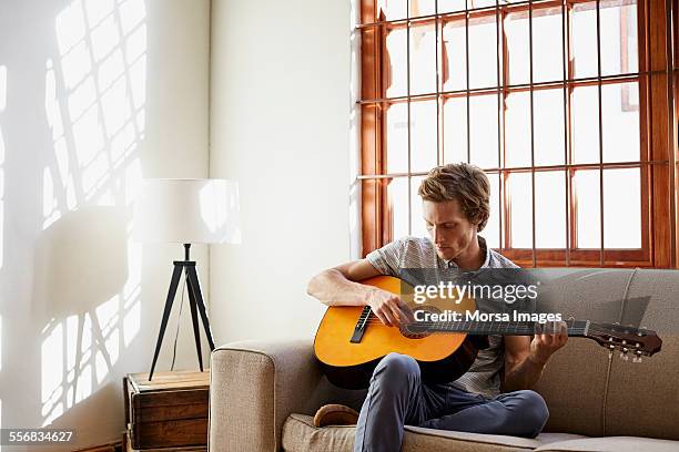 man playing guitar on sofa at home - acoustic guitar stock pictures, royalty-free photos & images