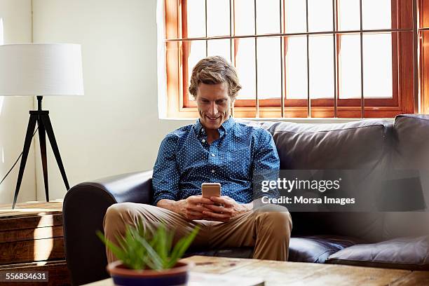 man using smart phone on sofa at home - mid adult stockfoto's en -beelden