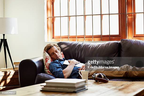man sleeping on sofa at home - sleeping man foto e immagini stock