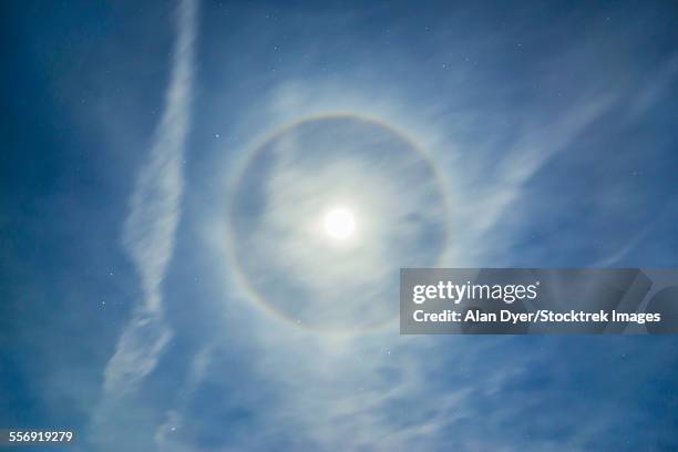 halo around full moon in a sky of cirrus clouds and contrails. - optical phenomenon halo stock pictures, royalty-free photos & images