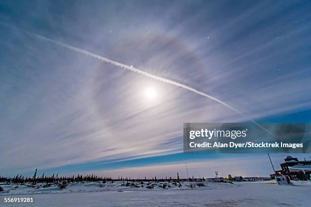 an ice crystal lunar halo around the gibbous moon with an aircraft jet contrail. - optical phenomenon halo stock pictures, royalty-free photos & images