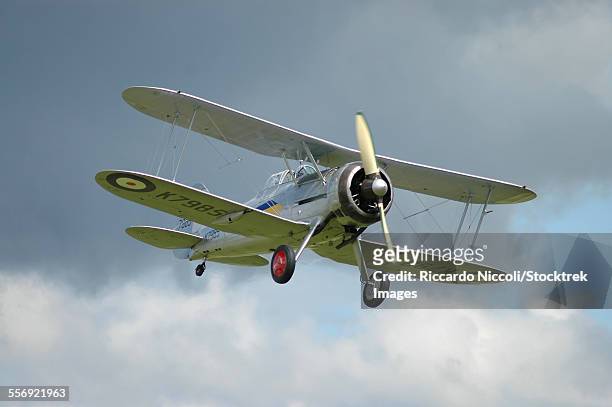 gloster gladiator in royal air force colors flying above duxford airport, england. - biplano foto e immagini stock
