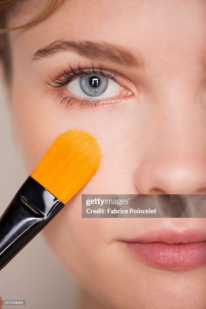 Beautiful woman applying make-up with a brush