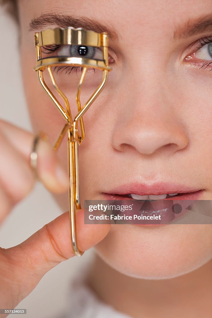 Young woman curling her eyelashes with a curler
