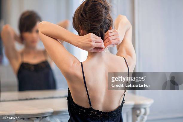 woman putting on necklace in front of mirror - halskette stock-fotos und bilder
