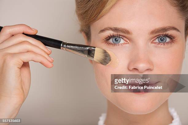 portrait of a beautiful woman applying foundation - applying makeup with brush foto e immagini stock