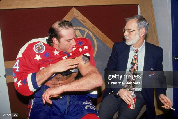 Al Iafrate of the Washington Capitals shows off his bicep tattoo to analyst Stan Fischler, who seems marginally interested and holds a cigarette and...