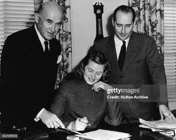 Swedish actress Ingrid Bergman sits at a desk and prepares to sign a document as Polish-born studio chief Samuel Goldwyn points with a letter opener...