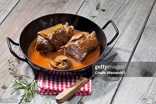 beef roulades in braising pan, rosmary, kitchen towel and knife on wood - braised stock pictures, royalty-free photos & images