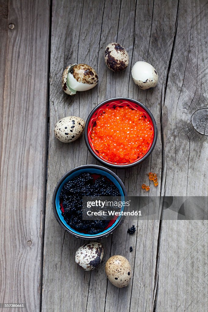 Black and red caviar in bowls, boiled quail eggs on wood