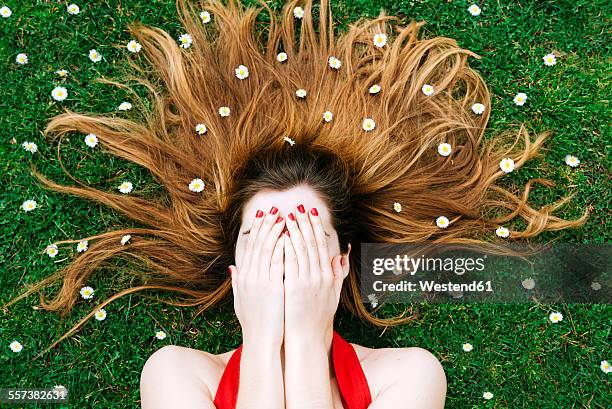 woman lying on grass in spring with hands on face and flowers on hair - blumen als accessoire stock-fotos und bilder