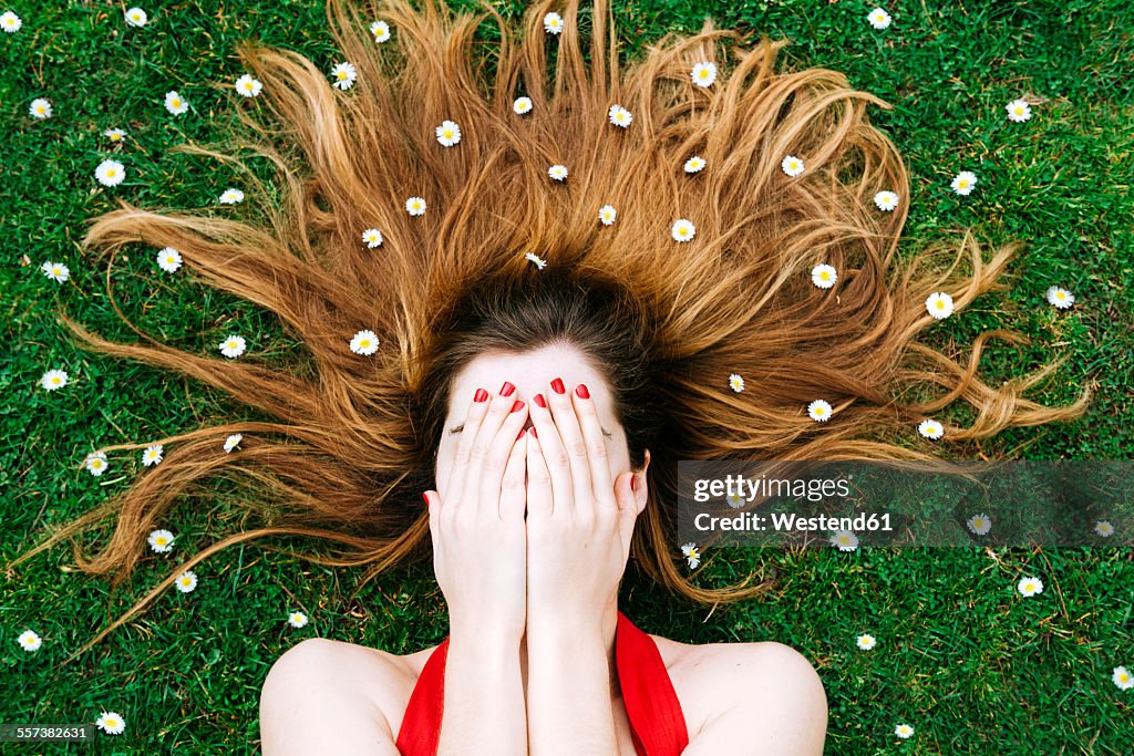 Woman lying on grass in spring with hands on face and flowers on hair