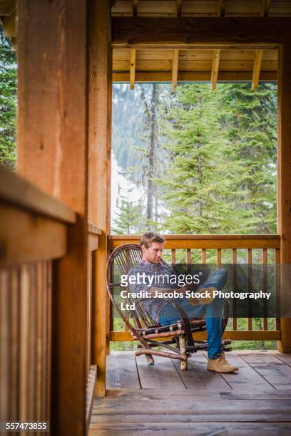 caucasian man reading in rocking chair on log cabin porch - rocking chair stock pictures, royalty-free photos & images