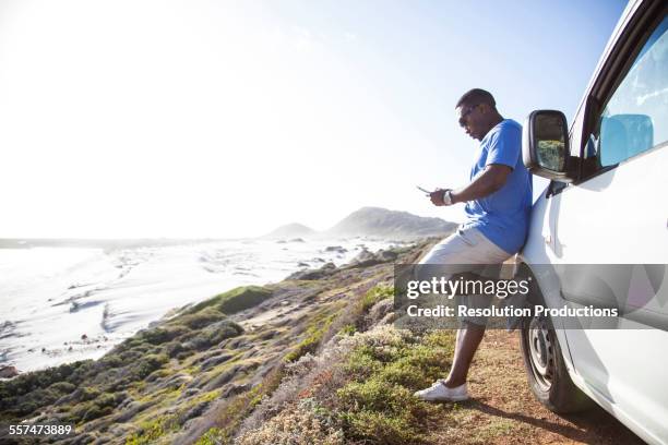 black man texting cell phone near car at coast - black shorts photos et images de collection