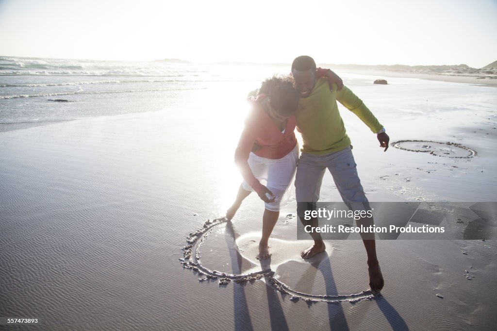 Couple drawing heart in sand on beach