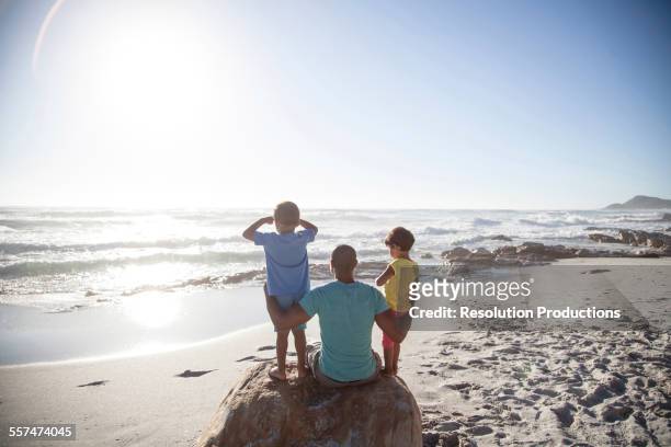 mixed race father and children sitting on beach - female looking away from camera serious thinking outside natural stock pictures, royalty-free photos & images