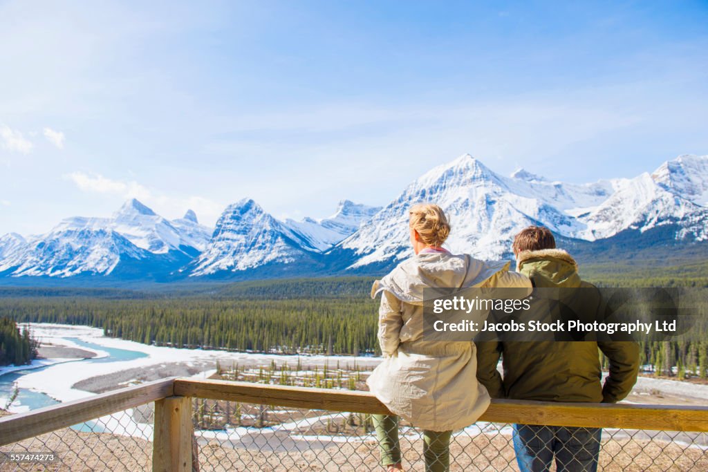 Caucasian couple admiring scenic view of snowy forest and mountains, Banff, Alberta, Canada