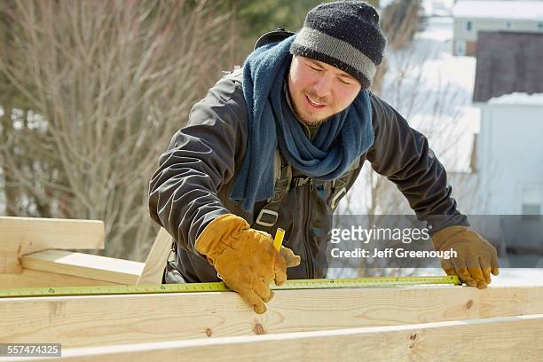 caucasian carpenter measuring wood planks in winter - glove stock-fotos und bilder