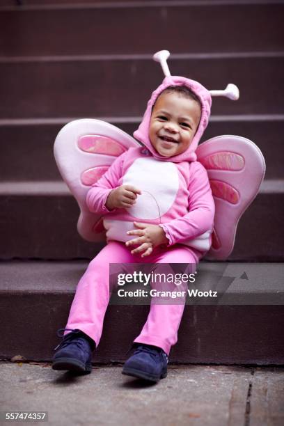 Mixed race girl wearing pink butterfly Halloween costume on staircase