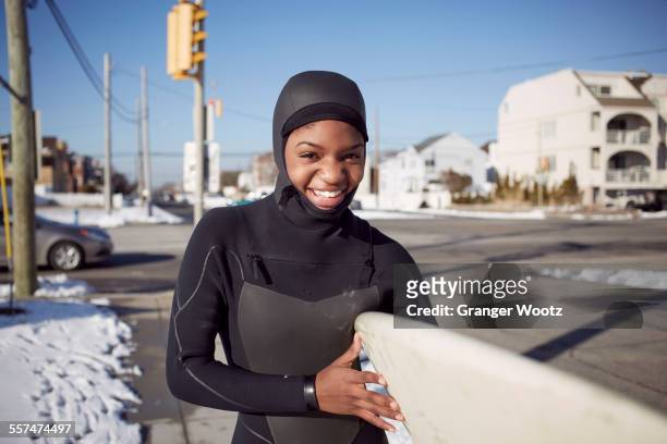 black teenage girl in wetsuit carrying surfboard in winter - long beach new york imagens e fotografias de stock