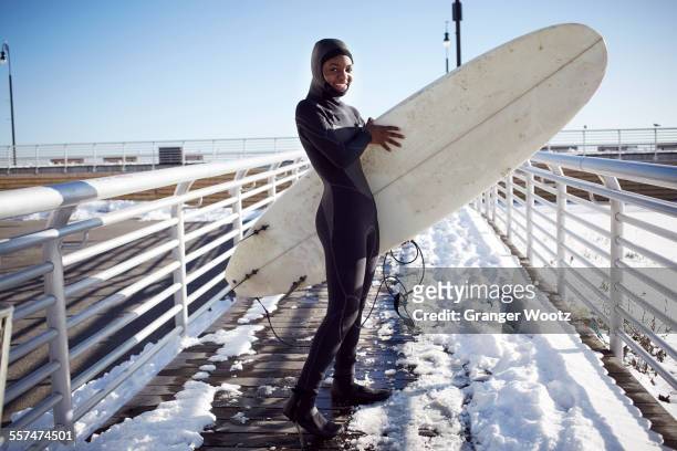 black teenage girl in wetsuit carrying surfboard in winter - long beach new york foto e immagini stock