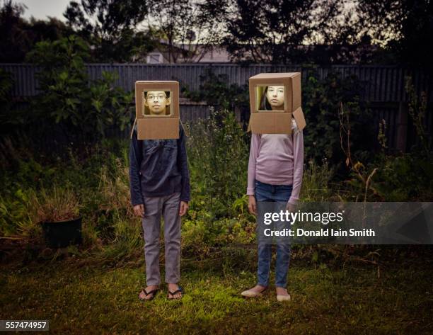 Mixed race children wearing cardboard astronaut helmets in backyard