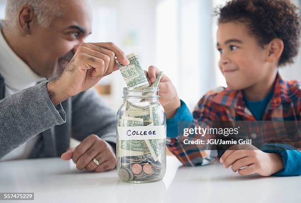 mixed race grandfather and grandson saving money in college fund jar - boys money stock pictures, royalty-free photos & images