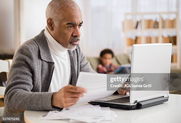 mixed race man paying bills on laptop - social projects address needs of struggling families stockfoto's en -beelden