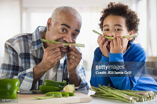 mixed race grandfather and grandson making mustaches with asparagus - portrait grimace photos et images de collection