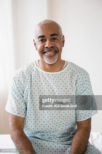 mixed race older man sitting on hospital bed - patient gown stock pictures, royalty-free photos & images