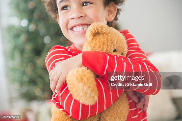 mixed race boy hugging teddy bear at christmas - pyjamas stock pictures, royalty-free photos & images