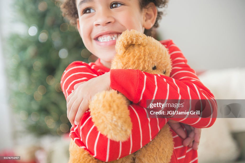 Mixed race boy hugging teddy bear at Christmas