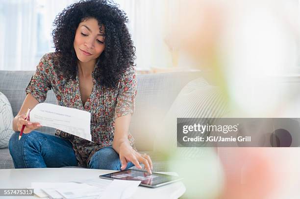 mixed race woman paying bills on digital tablet - financial planning home stock pictures, royalty-free photos & images