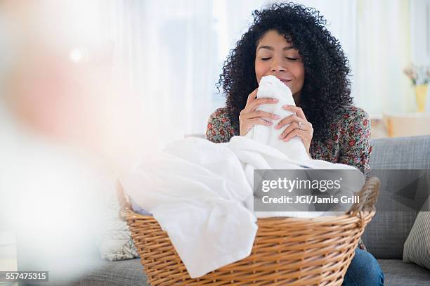 mixed race woman smelling clean towels in laundry - white laundry foto e immagini stock