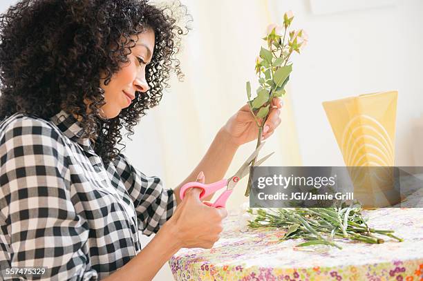 mixed race woman cutting flower stems at table - ent stockfoto's en -beelden