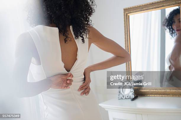 mixed race woman zipping dress in mirror - jurk stockfoto's en -beelden