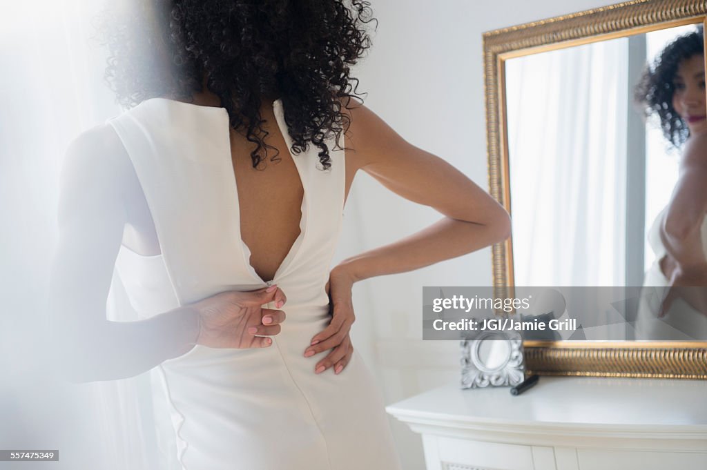 Mixed race woman zipping dress in mirror