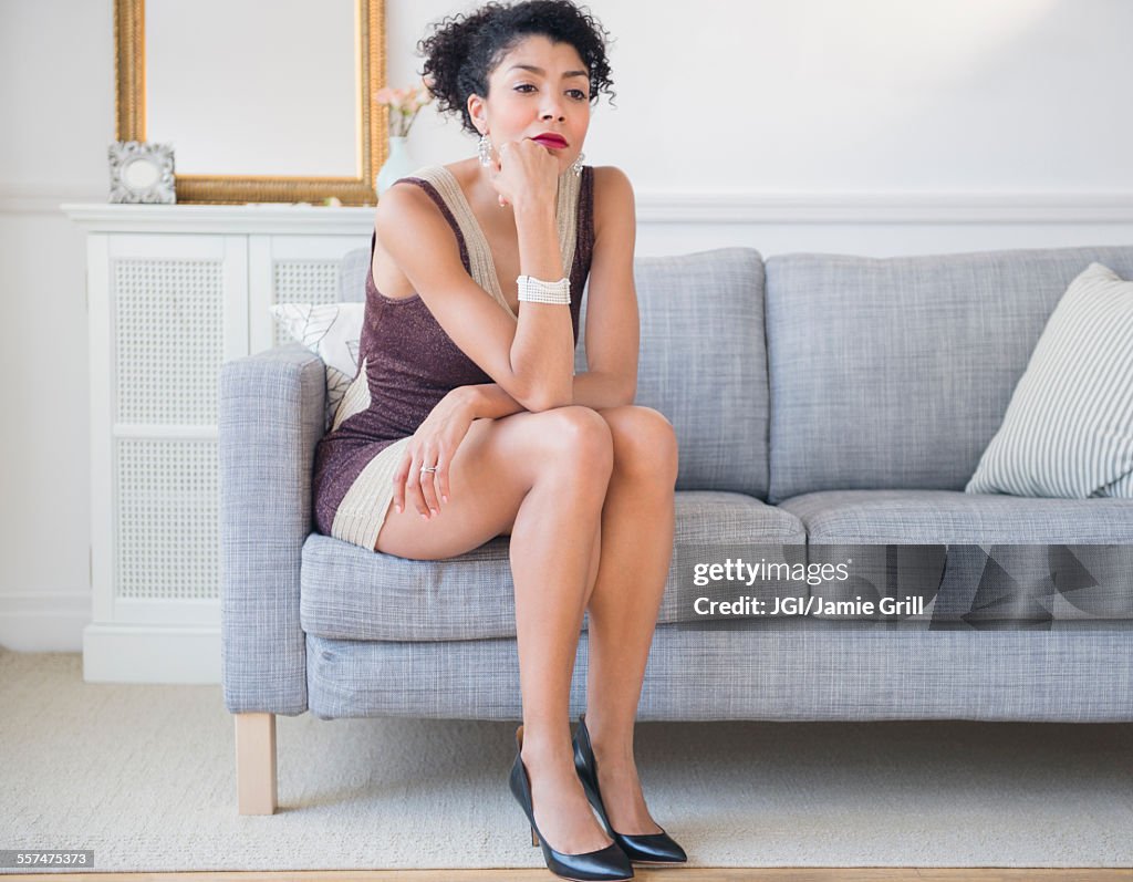 Mixed race woman in cocktail dress sitting on sofa