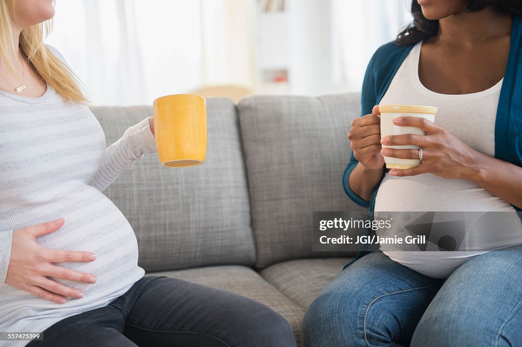 Pregnant women drinking coffee and talking on sofa