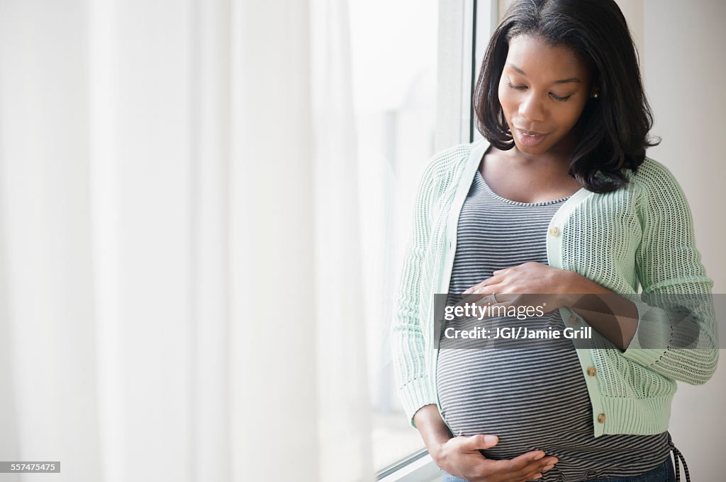 Black pregnant woman holding her stomach at window