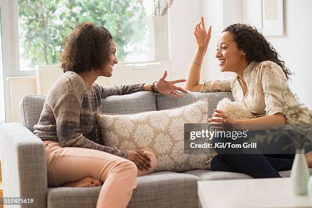 laughing women talking on sofa - two women talking stockfoto's en -beelden