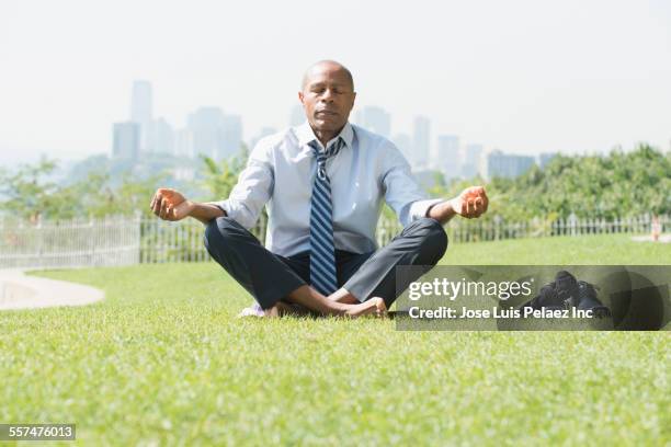 black businessman meditating on grass - mudra stock-fotos und bilder