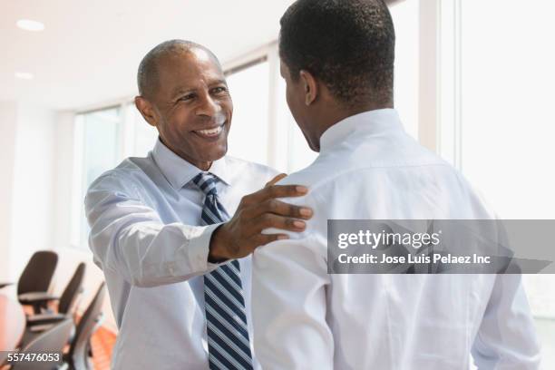 black businessmen talking in office - man touching shoulder stock-fotos und bilder